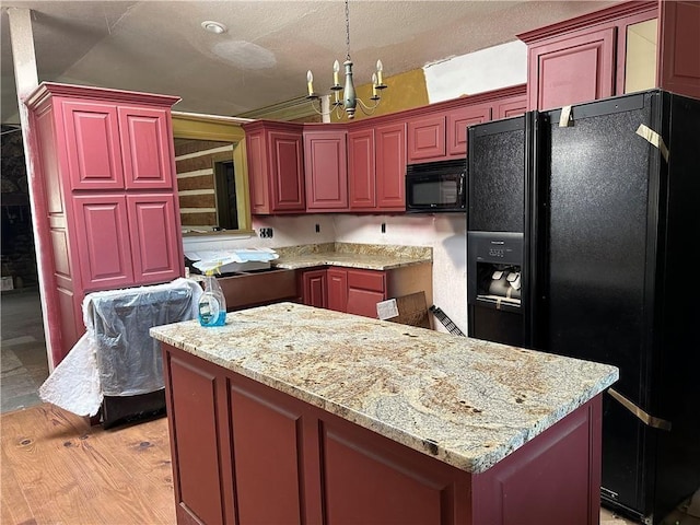 kitchen featuring light stone counters, light hardwood / wood-style flooring, black appliances, a kitchen island, and an inviting chandelier