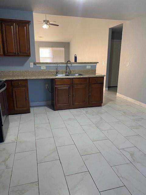 kitchen with a ceiling fan, light stone countertops, range, and a sink