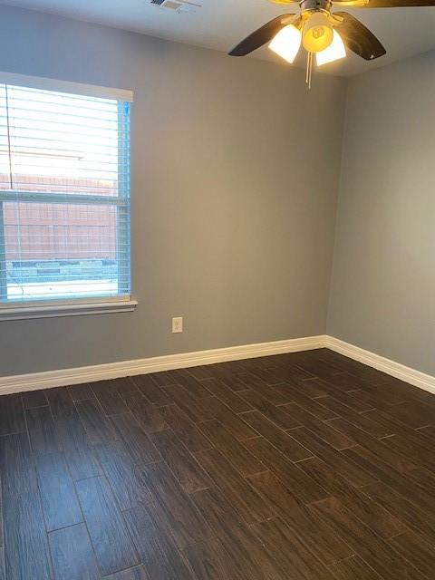 spare room featuring baseboards, dark wood-style floors, a ceiling fan, and visible vents