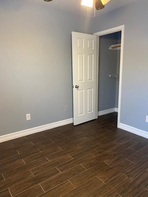 empty room with ceiling fan, baseboards, and dark wood-style floors