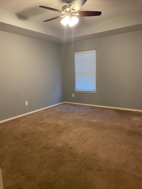 carpeted spare room featuring baseboards and a ceiling fan