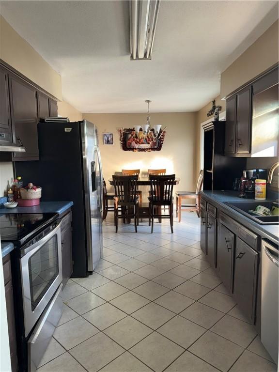 kitchen featuring stainless steel appliances, sink, an inviting chandelier, light tile patterned floors, and dark brown cabinetry