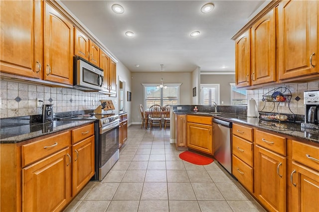 kitchen with stainless steel appliances, light tile patterned floors, dark stone counters, pendant lighting, and sink