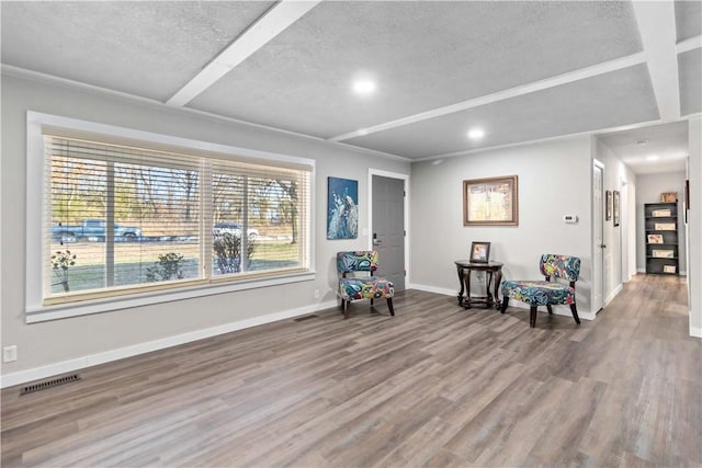 living area with a textured ceiling, wood finished floors, visible vents, and baseboards