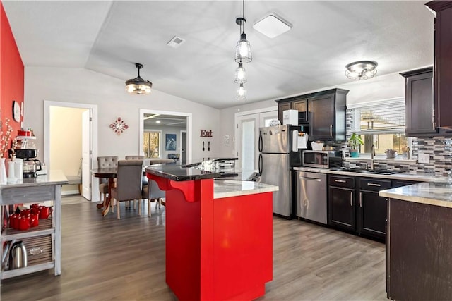 kitchen with visible vents, wood finished floors, vaulted ceiling, stainless steel appliances, and a sink