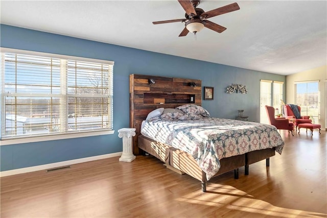 bedroom featuring a ceiling fan, visible vents, baseboards, and wood finished floors