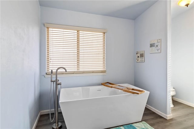 interior space featuring toilet, a freestanding bath, baseboards, and wood finished floors