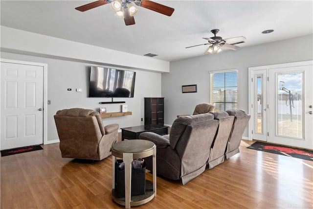 living room featuring a ceiling fan, visible vents, light wood-style flooring, and baseboards