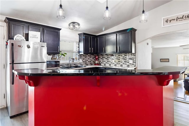 kitchen featuring decorative backsplash, appliances with stainless steel finishes, light wood-style floors, a sink, and a kitchen bar