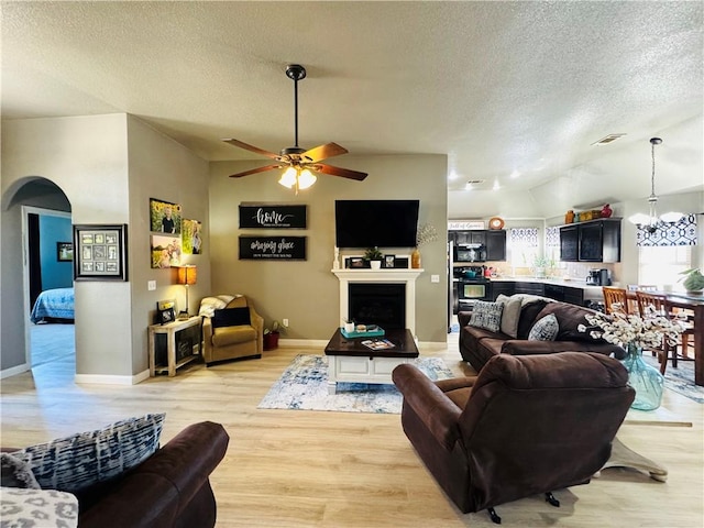 living area featuring arched walkways, ceiling fan with notable chandelier, light wood-style flooring, and a textured ceiling