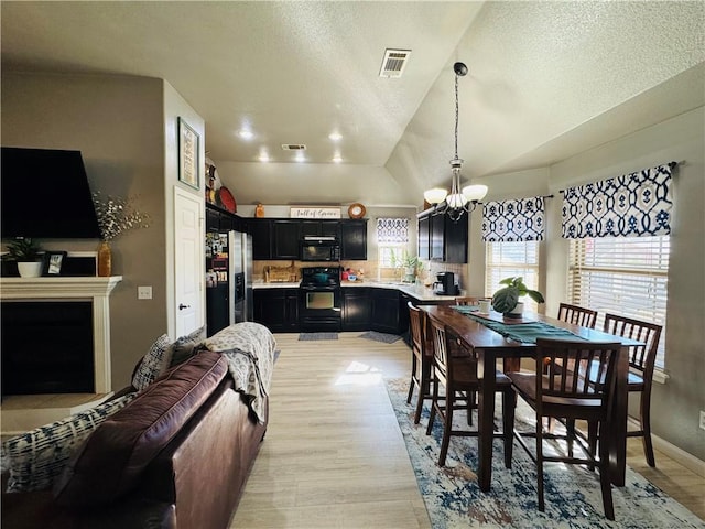 dining room featuring a notable chandelier, visible vents, a textured ceiling, and lofted ceiling