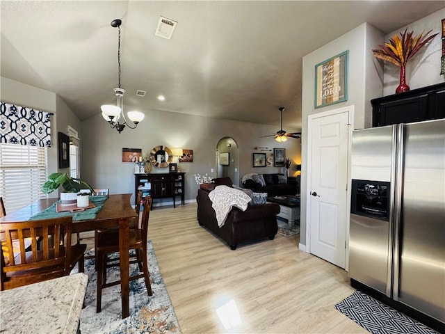 dining space with visible vents, light wood-style flooring, ceiling fan with notable chandelier, arched walkways, and vaulted ceiling