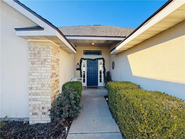 entrance to property featuring brick siding, stucco siding, and roof with shingles