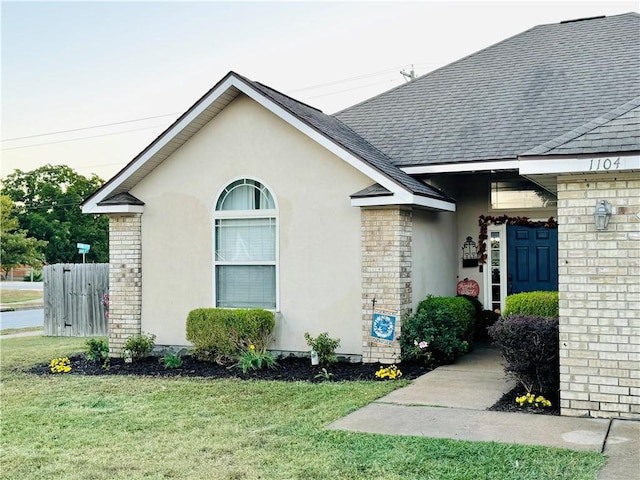 view of side of home featuring a shingled roof, a yard, fence, and stucco siding