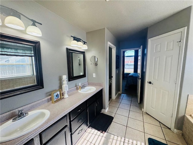 ensuite bathroom featuring tile patterned floors, double vanity, a textured ceiling, and a sink