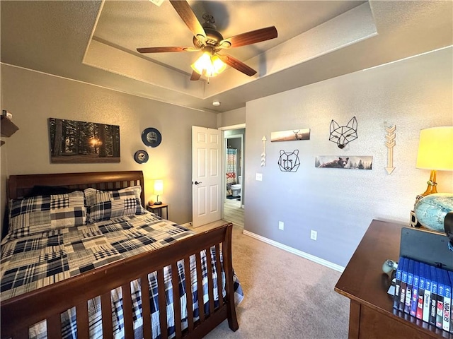 carpeted bedroom featuring a raised ceiling, baseboards, and ceiling fan