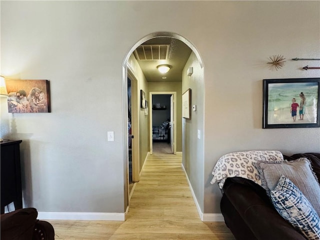 hall with arched walkways, visible vents, baseboards, and light wood-style floors