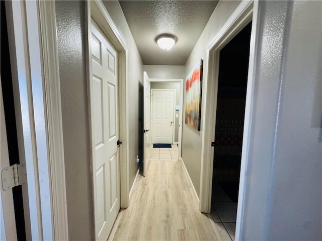 corridor with baseboards, light wood finished floors, and a textured ceiling