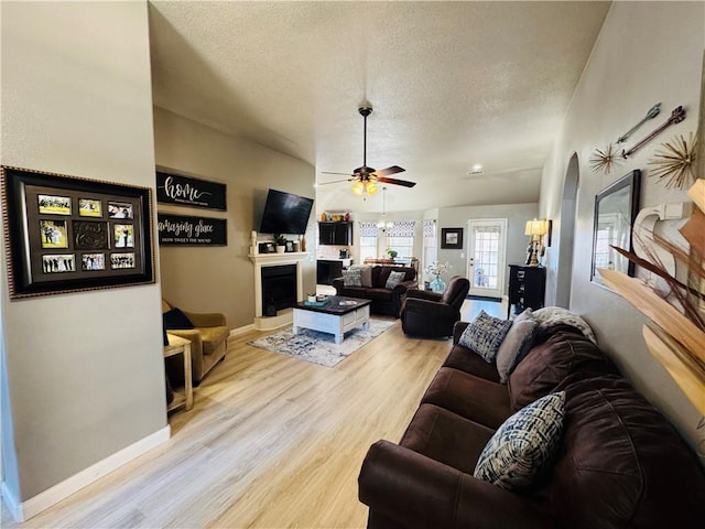 living room featuring ceiling fan, baseboards, a fireplace, wood finished floors, and a textured ceiling