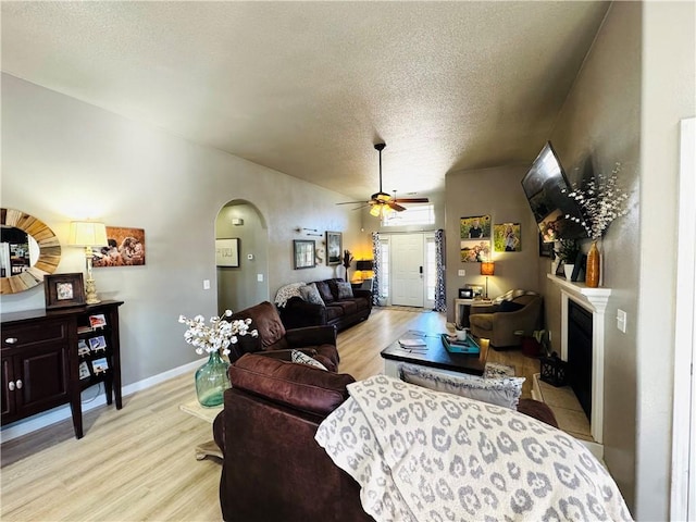 living area featuring a fireplace, arched walkways, light wood-type flooring, and a textured ceiling