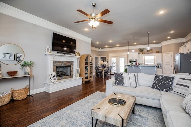 living room with a stone fireplace, ornamental molding, ceiling fan, and dark hardwood / wood-style floors