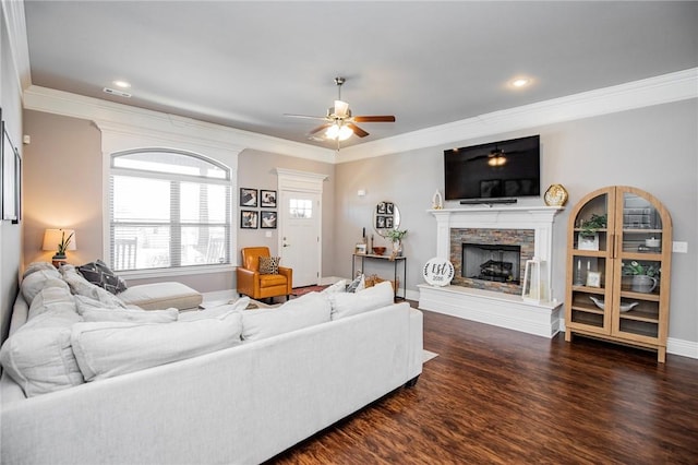 living room with ceiling fan, ornamental molding, dark hardwood / wood-style floors, and a stone fireplace