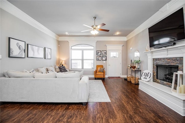 living room featuring ceiling fan, dark hardwood / wood-style flooring, a stone fireplace, and crown molding