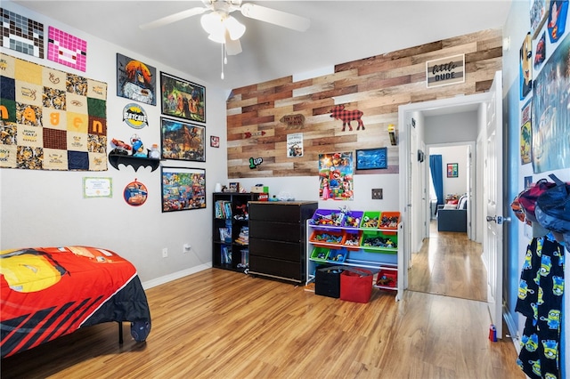 bedroom featuring ceiling fan, hardwood / wood-style floors, and wooden walls