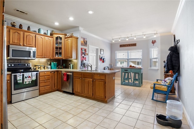 kitchen with appliances with stainless steel finishes, kitchen peninsula, ornamental molding, light tile patterned flooring, and backsplash