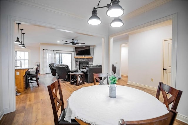 dining area featuring a fireplace, ceiling fan, light hardwood / wood-style floors, and crown molding