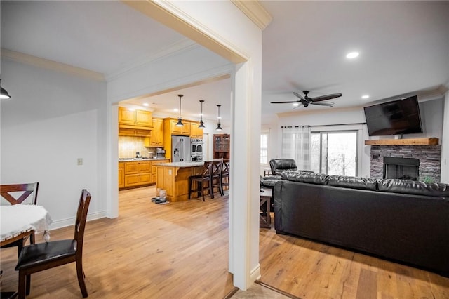 living room featuring a fireplace, light wood-type flooring, ceiling fan, and crown molding