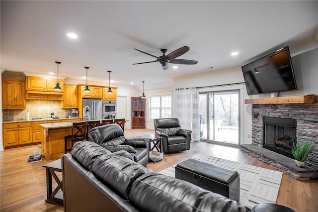 living room with ceiling fan, light hardwood / wood-style floors, a stone fireplace, and ornamental molding