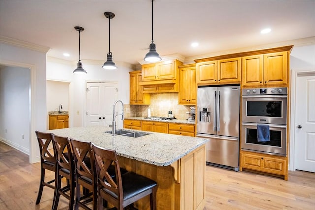 kitchen featuring appliances with stainless steel finishes, an island with sink, ornamental molding, light stone counters, and sink