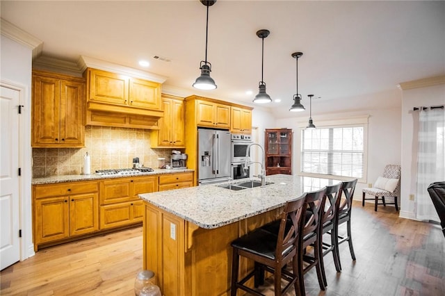 kitchen with appliances with stainless steel finishes, hanging light fixtures, an island with sink, light stone countertops, and sink