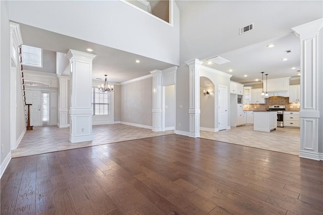 unfurnished living room featuring a towering ceiling, a chandelier, light hardwood / wood-style floors, and ornamental molding