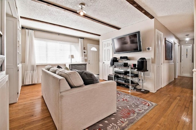 living room featuring light hardwood / wood-style floors, a textured ceiling, and beamed ceiling