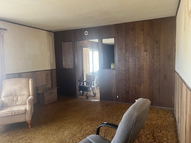 living area with wooden walls, a textured ceiling, and carpet floors