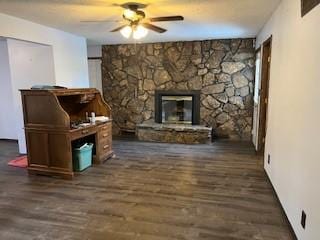 living room with dark wood-type flooring, ceiling fan, and a stone fireplace