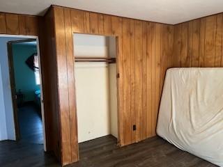 unfurnished bedroom featuring dark wood-type flooring, refrigerator, wooden walls, and a closet