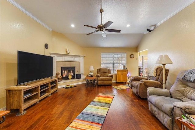 living room with vaulted ceiling, a tiled fireplace, crown molding, ceiling fan, and dark hardwood / wood-style flooring