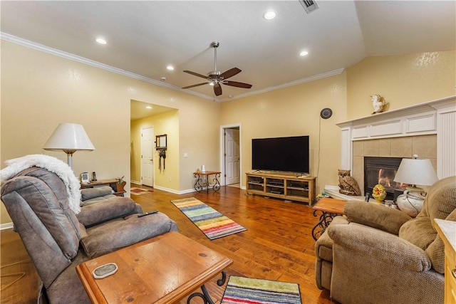 living room with vaulted ceiling, wood-type flooring, a tiled fireplace, crown molding, and ceiling fan