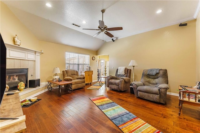 living room with dark wood-type flooring, ceiling fan, vaulted ceiling, and a tile fireplace