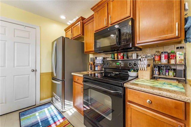 kitchen featuring black appliances, light stone counters, decorative backsplash, and light tile patterned floors