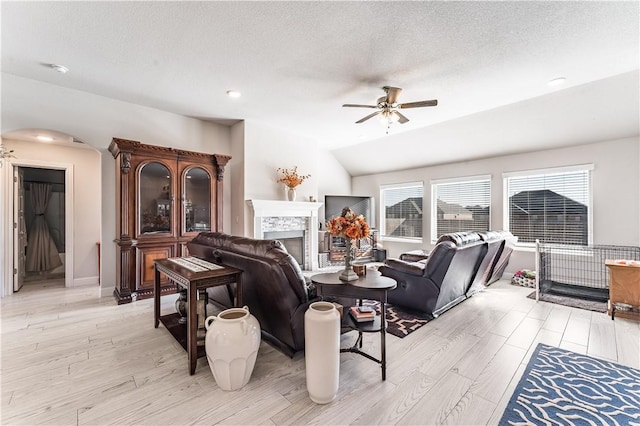 living room with a textured ceiling, ceiling fan, vaulted ceiling, and light hardwood / wood-style flooring