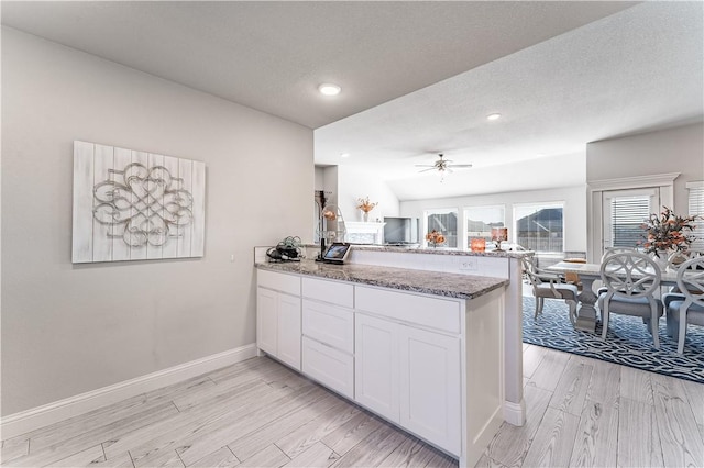 kitchen featuring white cabinetry, stone counters, ceiling fan, light hardwood / wood-style floors, and kitchen peninsula