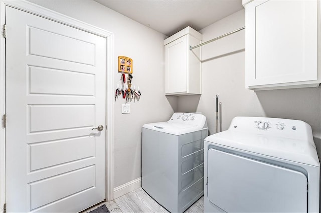 clothes washing area with washing machine and dryer, light hardwood / wood-style floors, and cabinets