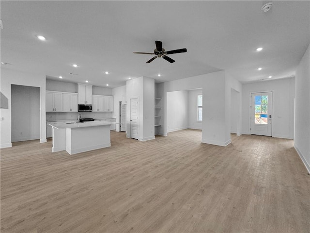 kitchen featuring a center island with sink, light wood-type flooring, ceiling fan, white cabinetry, and built in shelves