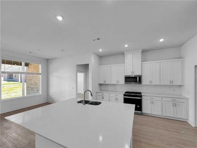 kitchen with appliances with stainless steel finishes, an island with sink, white cabinets, and sink