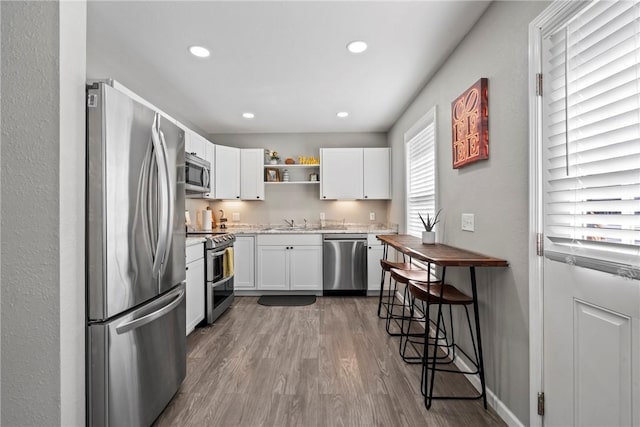 kitchen with hardwood / wood-style flooring, stainless steel appliances, a breakfast bar, white cabinetry, and sink