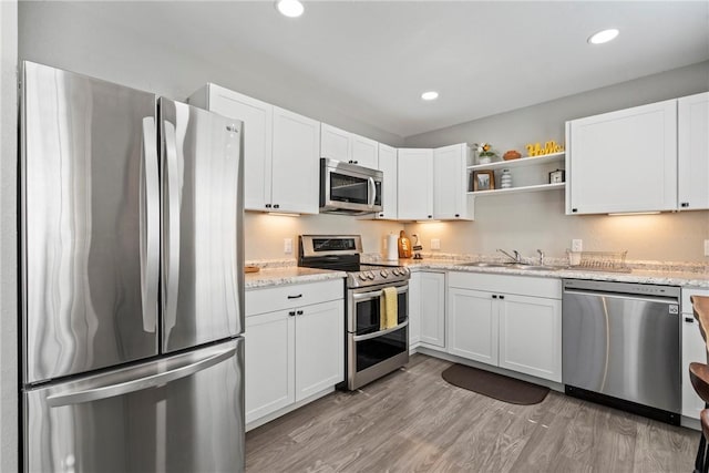 kitchen featuring light stone countertops, light hardwood / wood-style flooring, white cabinets, appliances with stainless steel finishes, and sink